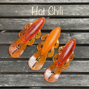 May include: Three plastic fishing lures in a "Hot Chili" color. The lures are orange and red with black flecks.
