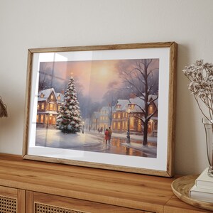 Puede incluir: Una pintura enmarcada de una escena de invierno en un pueblo cubierto de nieve, con un &aacute;rbol de Navidad iluminado en primer plano. La pintura presenta a una pareja caminando por la calle, casas con ventanas iluminadas y una farola.