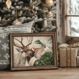 May include: A framed Christmas print depicts Santa Claus in a green suit and hat, nuzzling a reindeer. The print is in a brown frame, resting on a wooden surface. A gray pillow with snowflake embroidery and wrapped gifts are in the background.