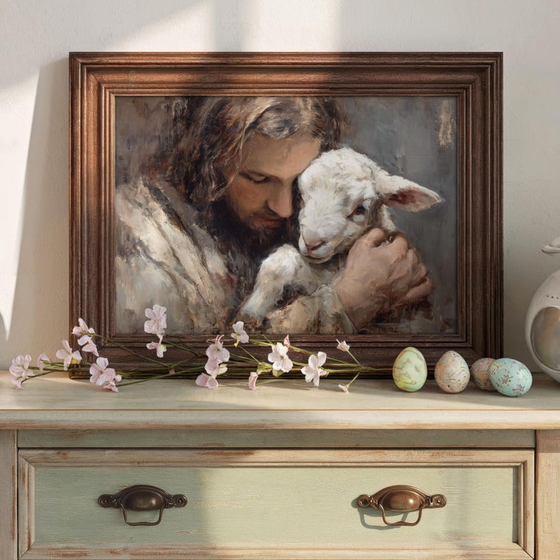 Pode incluir: Uma pintura emoldurada retrata um homem com cabelo comprido segurando ternamente um cordeiro. A obra de arte est&aacute; em uma moldura de madeira, com cores suaves e pinceladas. Ovos decorativos e flores cor-de-rosa est&atilde;o na superf&iacute;cie.