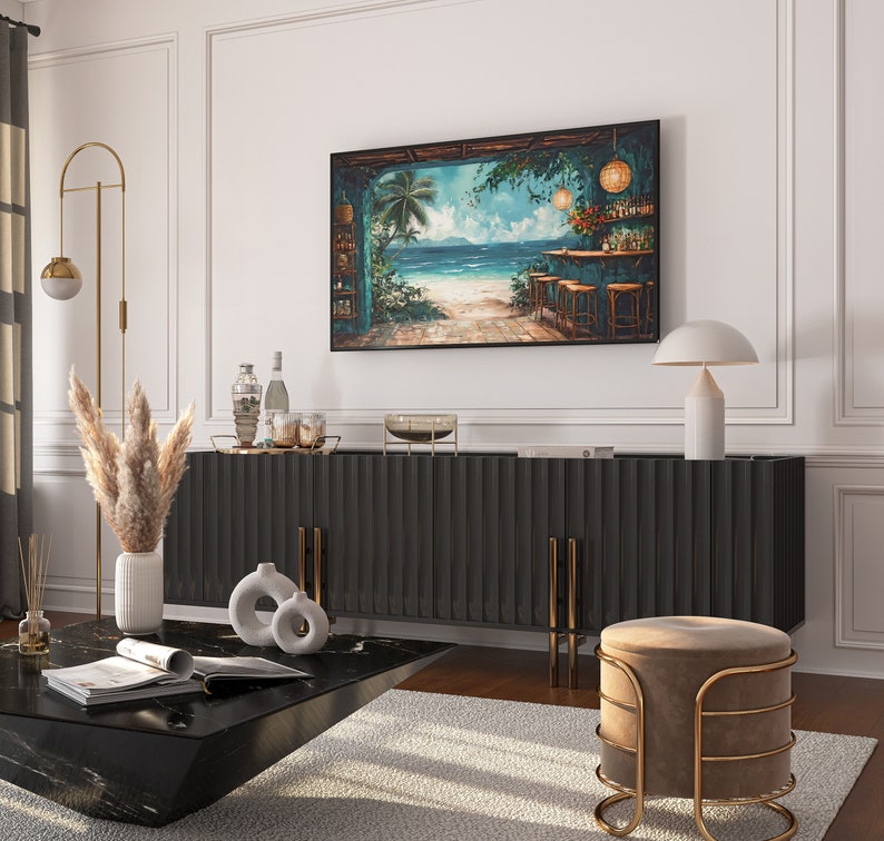 May include: A dark wood cabinet with a black top and gold accents. The cabinet has a tropical beach scene painting above it with a bar and palm trees. There is a white ceramic vase with dried pampas grass on the left side of the cabinet. A small round table with a black top and gold legs is in front of the cabinet. There is a white ceramic vase with a round shape on the table.