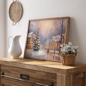 Puede incluir: Una pintura enmarcada de una escena de invierno con un pueblo nevado y un &aacute;rbol de Navidad iluminado en el centro. La pintura est&aacute; sobre una c&oacute;moda de madera con una jarra blanca y una cesta de mimbre con flores blancas.