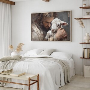 Pode incluir: Uma obra de arte emoldurada retrata uma pessoa com cabelo comprido abra&ccedil;ando ternamente um cordeiro. A obra de arte est&aacute; em uma moldura de madeira clara e pendurada acima de uma cama com roupa de cama branca. O quarto tem um design minimalista com tons neutros.