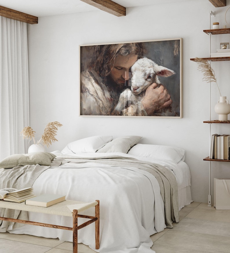 Pode incluir: Uma obra de arte emoldurada retrata uma pessoa com cabelo comprido abra&ccedil;ando ternamente um cordeiro. A obra de arte est&aacute; em uma moldura de madeira clara e pendurada acima de uma cama com roupa de cama branca. O quarto tem um design minimalista com tons neutros.