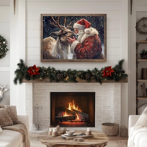 May include: A painting of Santa Claus with a white beard and red suit, kissing a brown and white deer on the nose. The painting is framed in wood and has a white background with snowflakes. The painting is hanging on a white wall above a fireplace with a garland of greenery and red poinsettias.