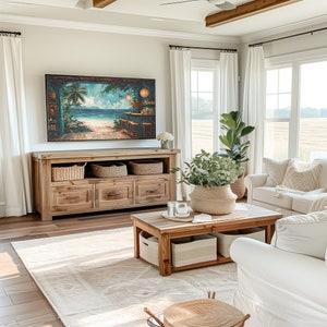 May include: A living room with white walls and a large, wooden entertainment unit with a flat-screen TV. The TV is displaying a tropical beach scene. There is a white sofa with cushions and a coffee table with a vase of greenery. The room is decorated with white curtains and a wooden ceiling beam.