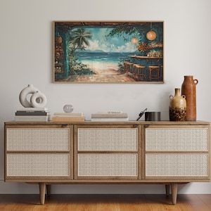 May include: A framed painting depicting a tropical bar scene with palm trees, a beach, and turquoise water. The bar has a thatched roof and is decorated with fairy lights. The painting is hanging on a white wall above a wooden cabinet with woven cane doors.