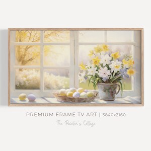 Puede incluir: Una pintura de una ventana con un jarrón de narcisos blancos y amarillos en un alféizar. Hay huevos de Pascua de colores pastel en una cesta en el alféizar de la ventana. La pintura está enmarcada en un marco de madera claro.