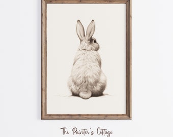 May include: A sepia-toned framed print featuring a detailed illustration of a rabbit from the rear. The rabbit has long ears and fluffy fur. The frame is made of wood. The text "The Painter's Cottage" is at the bottom.