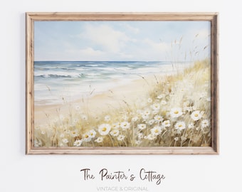 May include: A framed painting of a beach scene with white daisies in the foreground and a blue ocean in the background. The painting is titled "The Painter's Cottage, Vintage & Original Art Collective."