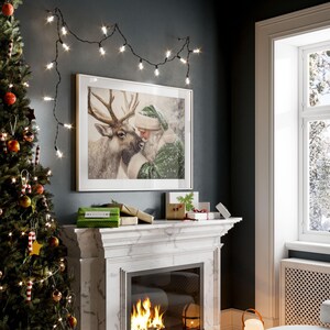 May include: A framed Christmas print depicts Santa Claus embracing a reindeer, set above a fireplace with a lit fire. A Christmas tree with ornaments and string lights is on the left. Several wrapped gifts and a string of lights are also visible.