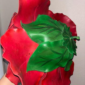 K&ouml;nnte beinhalten: Eine gro&szlig;e, rote Stoffrose mit gr&uuml;nen Bl&auml;ttern. Die Rose besteht aus mehreren Stoffschichten und hat einen gekr&auml;uselten Rand.