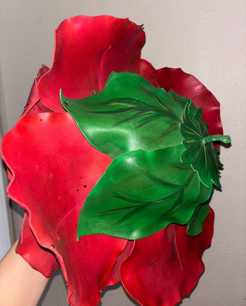 K&ouml;nnte beinhalten: Eine gro&szlig;e, rote Stoffrose mit gr&uuml;nen Bl&auml;ttern. Die Rose besteht aus mehreren Stoffschichten und hat einen gekr&auml;uselten Rand.