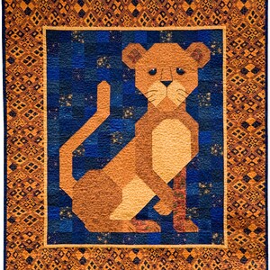 Op de afbeelding: Een bruin en tan leeuwenwelpje op een blauwe achtergrond. De leeuwenwelp is gemaakt van stof en is een patchwork ontwerp. De achtergrond is een blauw en goud patchwork ontwerp.