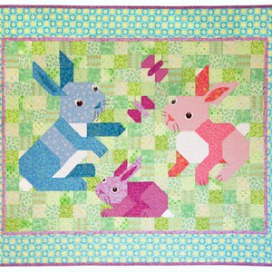 May include: A patchwork quilt with a green background features three bunnies. The bunnies are made of fabric in shades of blue, pink, and purple. The quilt is surrounded by a border of blue and green floral fabric.