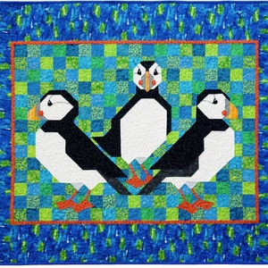 May include: Three colorful puffins with black and white bodies and orange beaks are arranged in a triangular pattern on a green and blue patchwork quilt. The puffins are surrounded by a red border and a blue border with white accents.