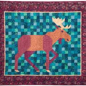 May include: A quilt featuring a brown moose with a large antler set against a blue and green patchwork background. The quilt is framed with a burgundy border with a floral pattern.