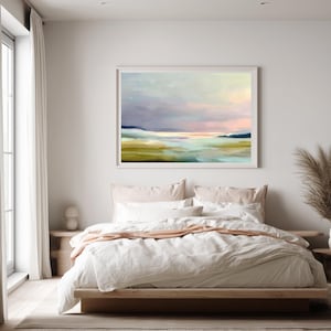 May include: A framed landscape painting with a soft, pastel color palette. The artwork depicts a serene scene with a body of water, rolling hills, and a cloudy sky. The painting is displayed above a bed with white linens.