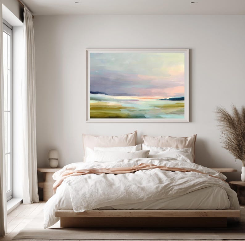 May include: A framed landscape painting with a soft, pastel color palette. The artwork depicts a serene scene with a body of water, rolling hills, and a cloudy sky. The painting is displayed above a bed with white linens.