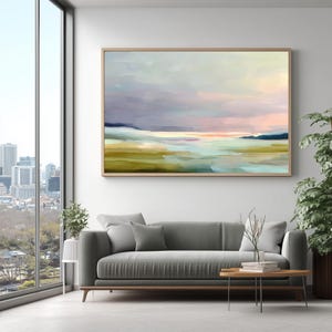 May include: Abstract landscape painting in a wooden frame. The artwork features a serene scene with a blend of colors, including blues, greens, and pinks, evoking a sense of calm. The painting is displayed above a gray sofa.