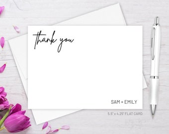May include: A white thank you card with black calligraphy that says "thank you". The card is 5.5 inches by 4.25 inches and is a flat card. The card is on a white wooden surface with a white envelope and a silver pen.
