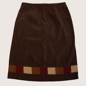 May include: A-line skirt in a deep brown colour. The skirt has a decorative band at the hem with alternating squares of brown, beige, and burgundy. The skirt is made of a soft, velvety material.