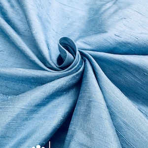 May include: Light blue fabric with a subtle sheen, artfully draped and swirled. The fabric's texture is visible, with a soft, flowing appearance. The text "marce and emma" is displayed with a floral logo.