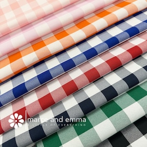 May include: A stack of eight gingham fabric swatches in various colors, including pink, orange, blue, red, navy, green, and black. The fabric is white with colored squares. The fabric is folded in a stack, with the top of the stack showing the pink fabric. The bottom of the stack shows the black fabric. The fabric is labeled "marc and emma a little of everything".
