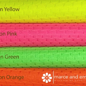 May include: Four rolls of neon colored mesh fabric. The rolls are stacked on top of each other. The colors are neon yellow, neon pink, neon green, and neon orange. The fabric has a small, repeating pattern of holes.