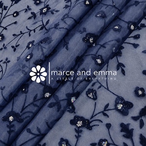 May include: A sheer navy blue fabric featuring a dark blue velvet floral vine pattern with small silver sequins at the center of each flower. The fabric is overlaid with a white logo that reads marce and emma A LITTLE OF EVERYTHING.
