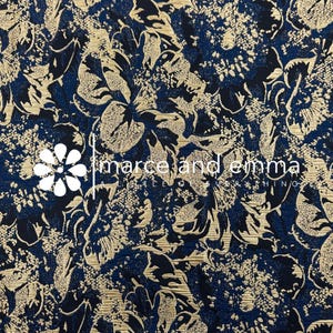 May include: A navy blue fabric with a floral pattern in gold and black. The fabric has a textured appearance, with the words "marce and emma" in white text. The floral design is detailed and covers the entire surface.