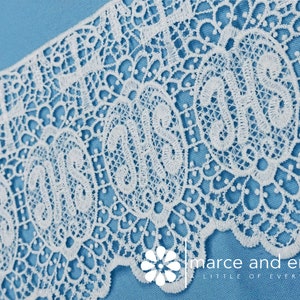 May include: White lace trim with a delicate floral pattern. The lace is on a blue background.