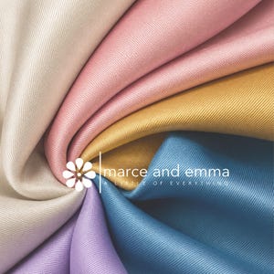 May include: A collection of smooth, satin-like fabric swatches in cream, pink, gold, blue, and lavender, arranged in a spiral pattern. The logo for marce and emma A LITTLE OF EVERYTHING is centered over the fabric with a white flower icon.