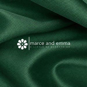 May include: A dark green fabric with a fine, textured weave and soft folds. Overlaid in white is a logo featuring a stylized flower icon next to the text marce and emma and the smaller tagline A LITTLE OF EVERYTHING centered below the brand name.