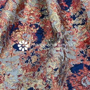 May include: A piece of fabric featuring a textured, metallic pattern in gold and copper tones layered over a deep navy blue base. The surface has a raised, intricate design with a visible white logo and the text marce and emma printed on it.