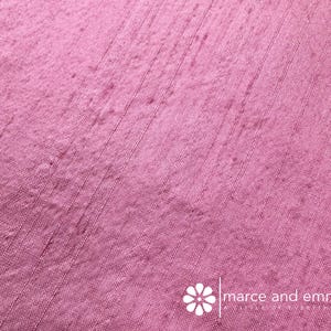 May include: Close-up of a textured, pink fabric with vertical lines. The fabric has a slightly uneven surface and a subtle sheen. The bottom right corner features the text "marce and emma".
