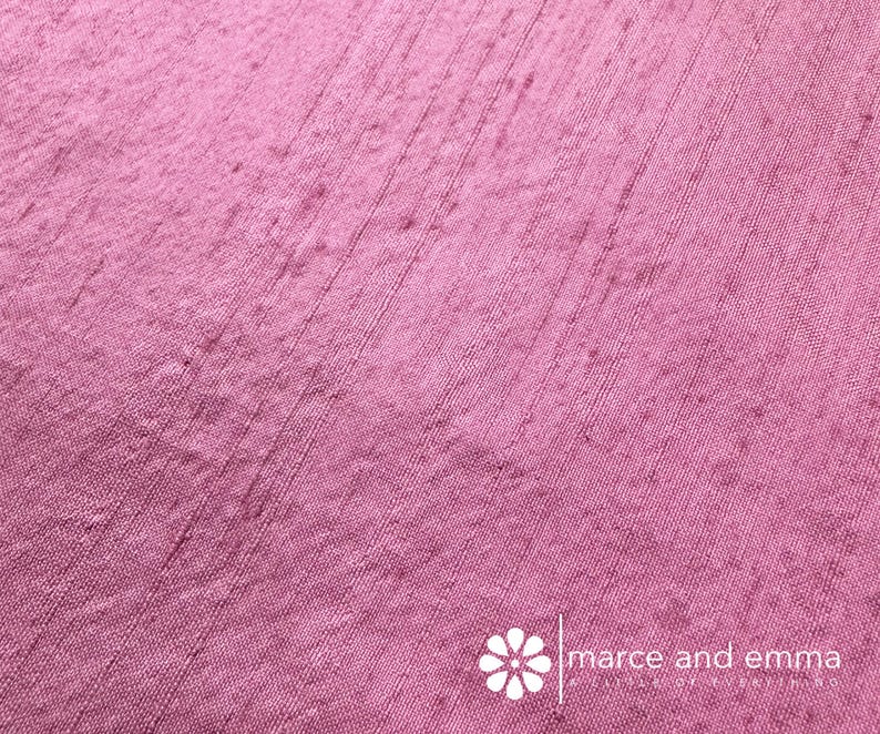 May include: Close-up of a textured, pink fabric with vertical lines. The fabric has a slightly uneven surface and a subtle sheen. The bottom right corner features the text "marce and emma".