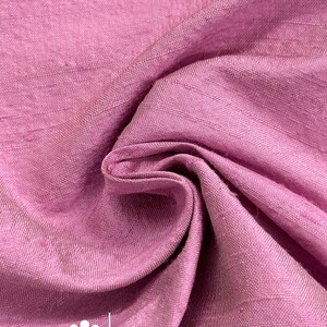 May include: Close-up of a folded, textured fabric in a dusty rose color. The fabric has a subtle sheen and visible weave. The text "marce and emma" is printed on the fabric.