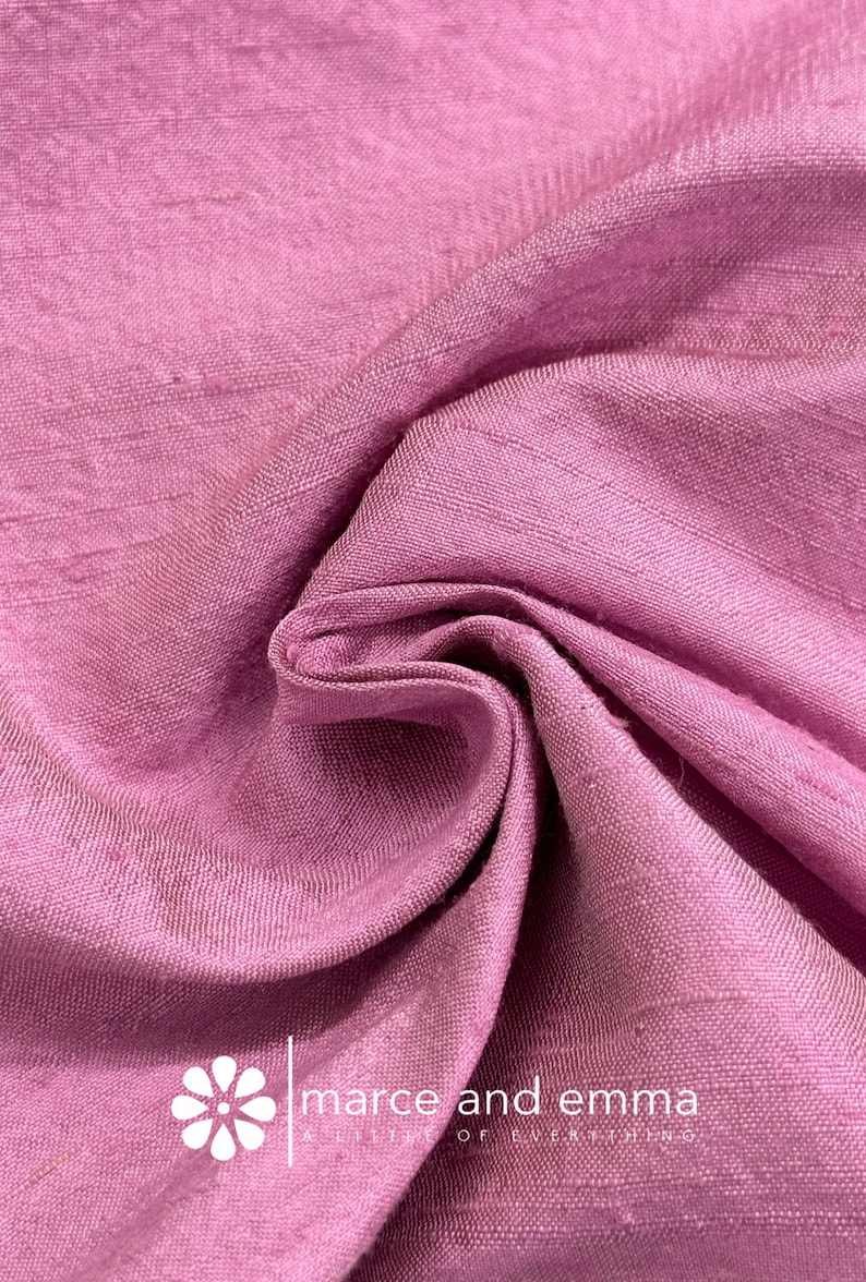 May include: Close-up of a folded, textured fabric in a dusty rose color. The fabric has a subtle sheen and visible weave. The text "marce and emma" is printed on the fabric.