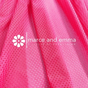 May include: Pink mesh fabric with a gradient from light pink to dark pink. The fabric has a small, repeating pattern of holes. The text "marce and emma a little of everything" is printed on the fabric.