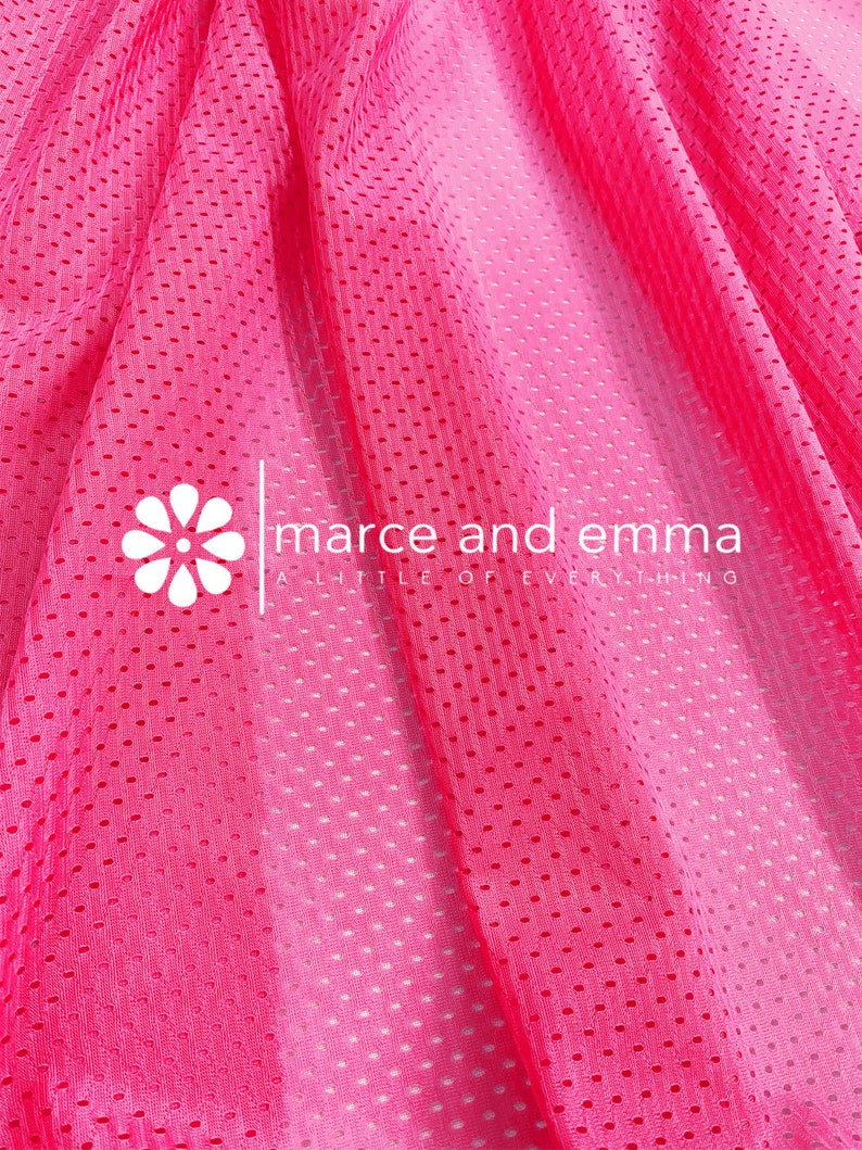 May include: Pink mesh fabric with a gradient from light pink to dark pink. The fabric has a small, repeating pattern of holes. The text "marce and emma a little of everything" is printed on the fabric.