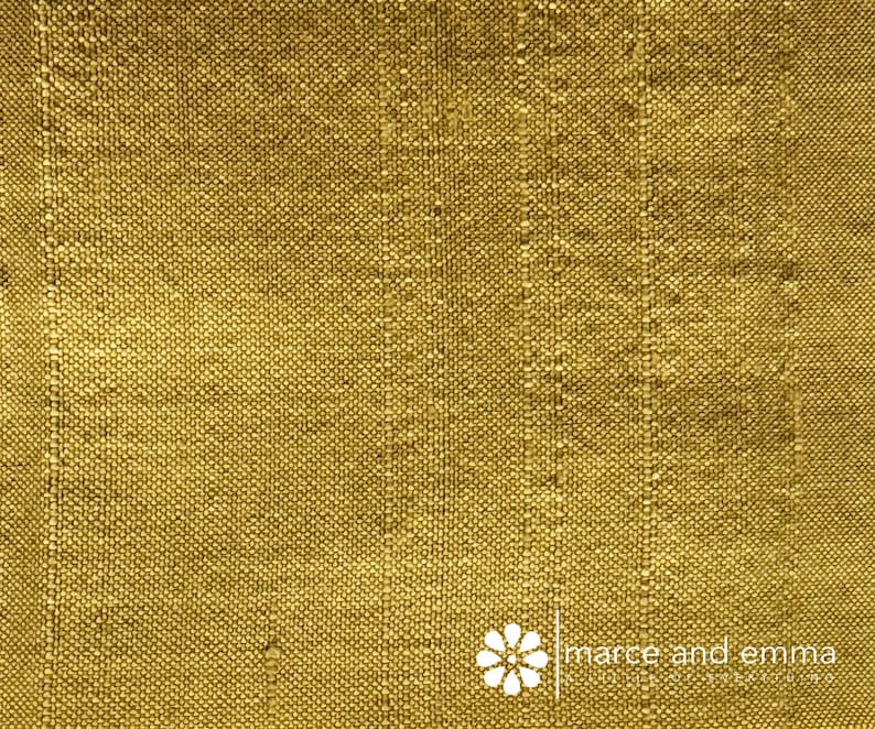 May include: Close-up of a textured, golden-yellow fabric. The weave is visible, with vertical lines creating a subtle striped effect. The fabric has a slightly rough appearance. The logo "marce and emma" is in the bottom right corner.