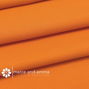 May include: Close-up of a bright orange fabric with a subtle textured weave. The fabric is folded in layers, showcasing its smooth and soft texture.
