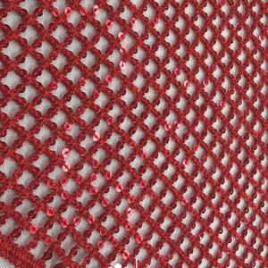 May include: Close-up of a red crocheted fabric with a diamond pattern. Small, shiny red sequins are interspersed throughout the design. The fabric has a textured appearance and is likely used for decorative purposes.