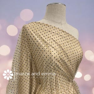 May include: A beige fabric with a polka dot pattern, draped over a mannequin. The dots are a mix of black and gold. The text "marce and emma" is visible on the fabric.