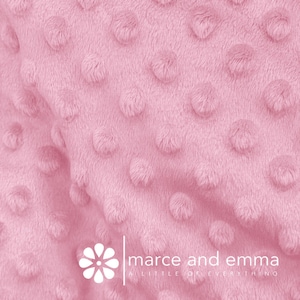 May include: Close-up of a soft, pink, textured fabric with a subtle, raised dot pattern. The fabric is known as "minky" and is often used for blankets, baby clothes, and other soft goods.