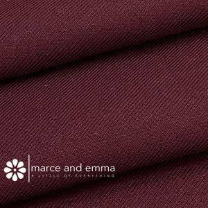 May include: Close-up of a deep burgundy fabric with a subtle diagonal weave. The fabric is smooth and has a soft, luxurious feel.