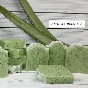 May include: A stack of green and white soap bars with a speckled texture. The soap bars are labeled "ALOE & GREEN TEA".