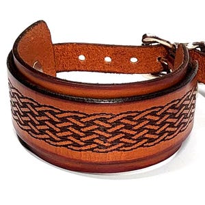 May include: A brown leather cuff bracelet with a woven design. The bracelet features a buckle closure and is made of a thick, sturdy leather. The woven pattern is dark brown, and the overall style is rustic and handcrafted.