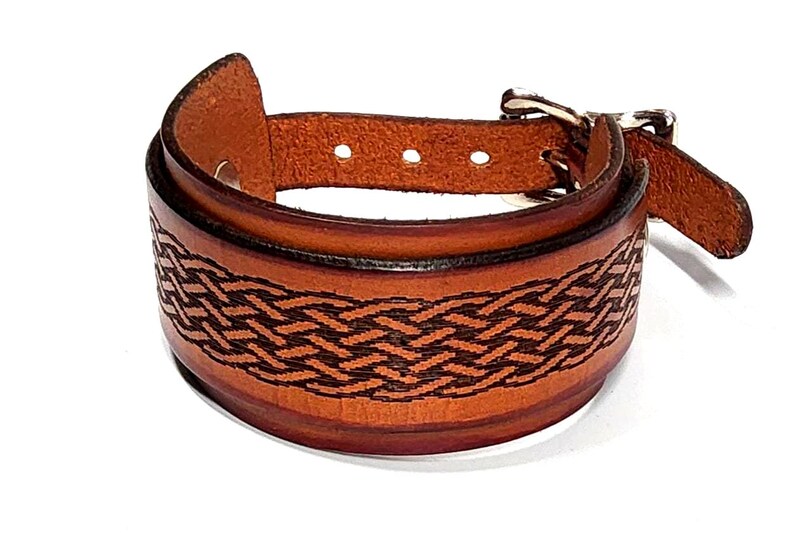 May include: A brown leather cuff bracelet with a woven design. The bracelet features a buckle closure and is made of a thick, sturdy leather. The woven pattern is dark brown, and the overall style is rustic and handcrafted.